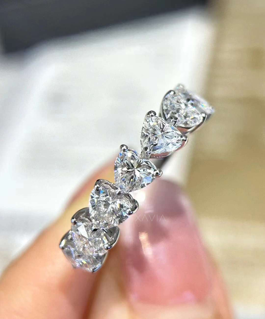 Close-up of floating heart lab-grown diamonds prong-set in eternity band, held between fingers